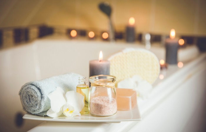 spa-like bath tub covered with candles, tray holds towel, bath salts, soap and flower