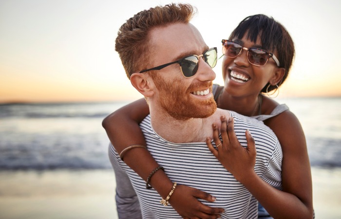 Interracial couple embracing on the beach, wearing sunglasses
