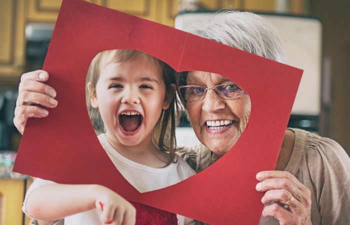 Grandmother with grandchild holding piece of construction paper with a heart cutout