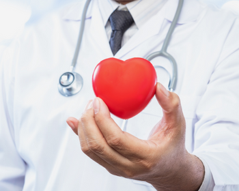 Doctor in white coat with stethoscope holding up a red heart