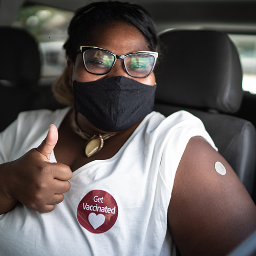 African American female smiling, wearing mask, giving a thumbs up