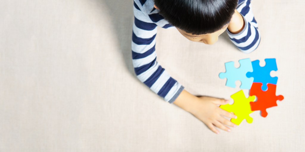 Autistic Asian boy put head on hand, holding colorful jigsaw puzzle as symbol of autism spectrum for World Autism Awareness day.