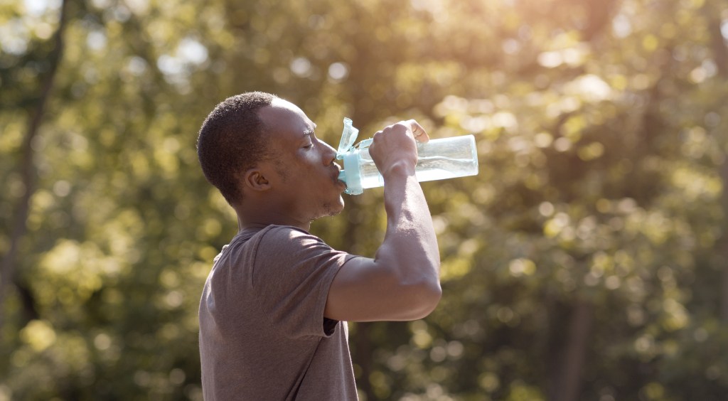 Overheated African American male drinking water from bottle in park