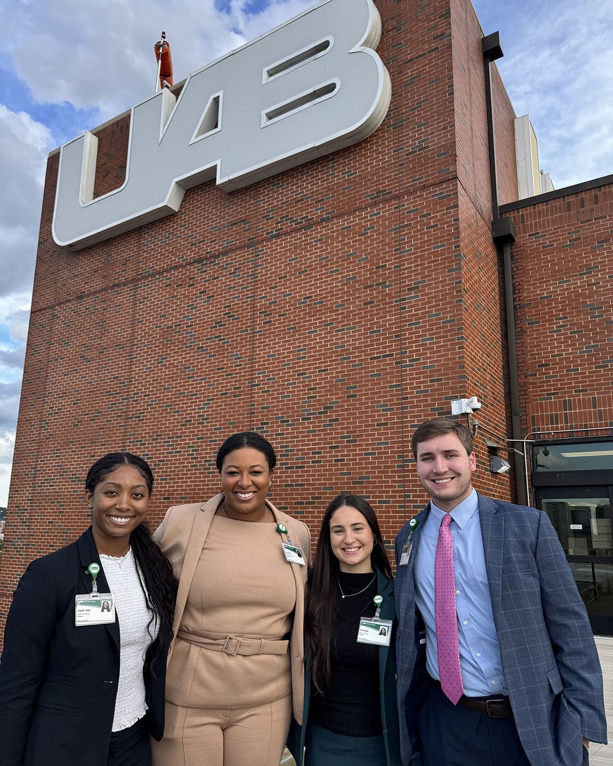 Group of individuals standing and smiling in front of UAB sign