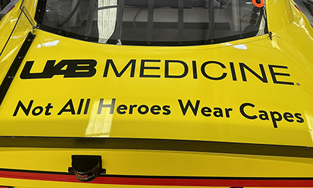 UAB Medicine logo and phrase "Not All Heroes Wear Capes" on yellow race car