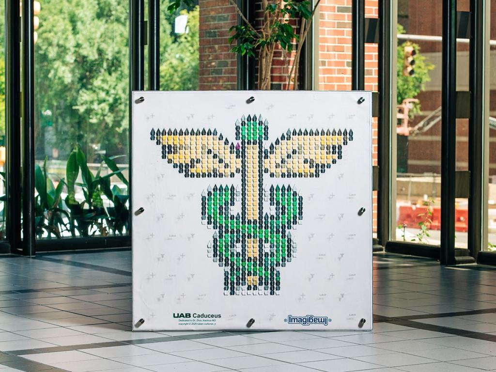 An artwork by Vuittonet with 586 green, gold and white folded cranes similar to pixels that make up a picture, secured to a 4-by-4-foot canvas to create the caduceus.
