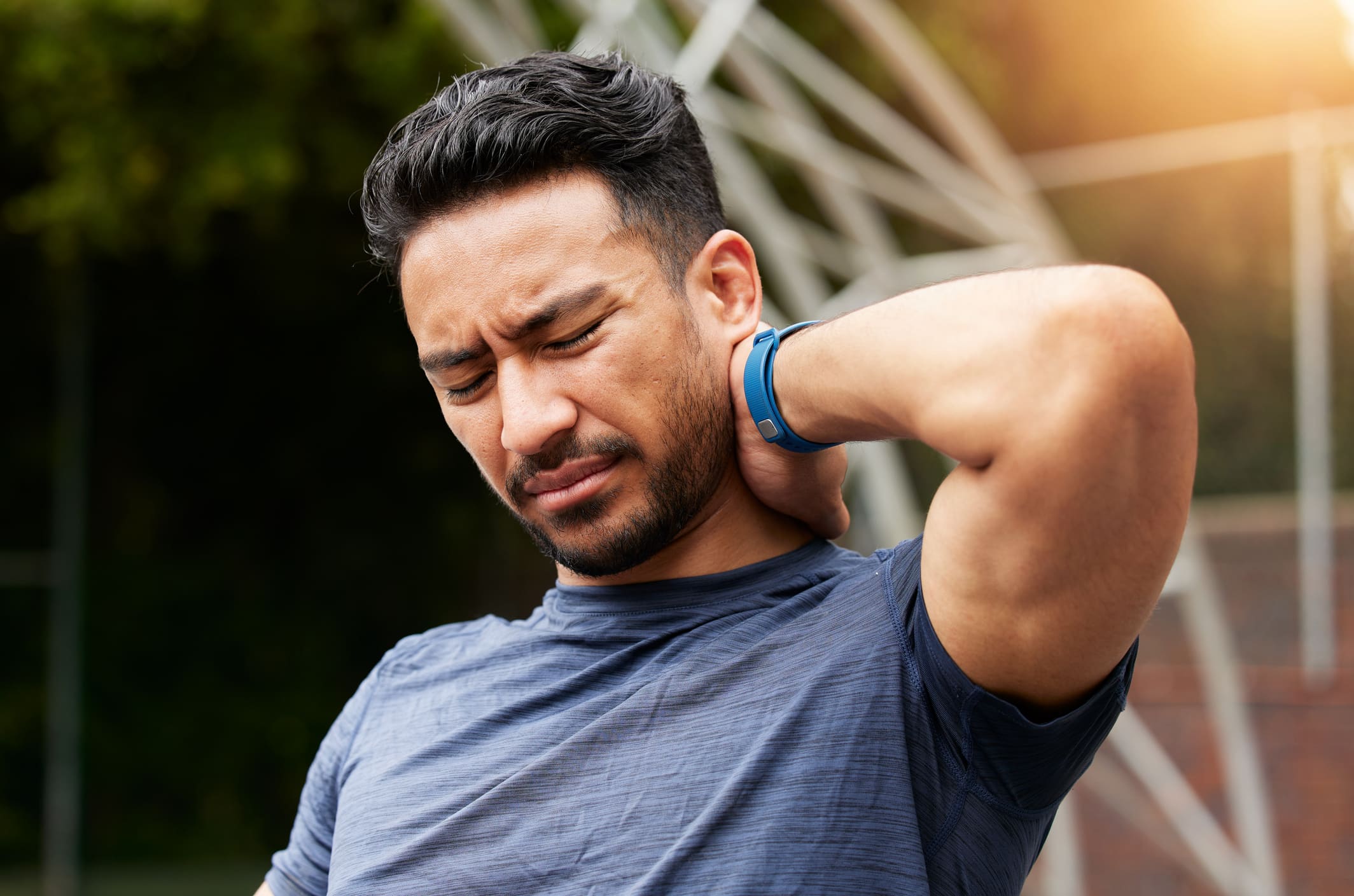 Athletic Asian man holding neck with his hand, indicating neck pain or injury.
