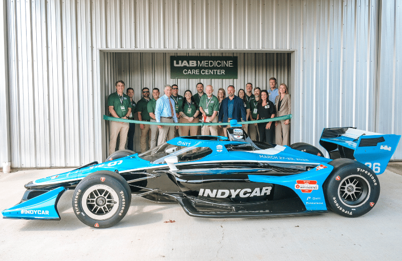 UAB Medicine care team cutting a green ribbon with a blue race car infront of them