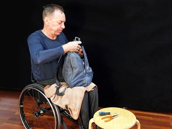 A man in a wheelchair holds a backpack in his hands