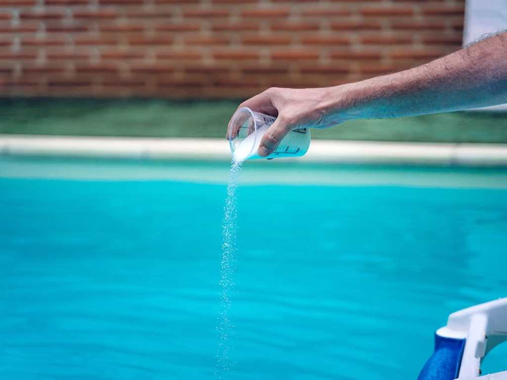 hand pouring chlorine into a pool
