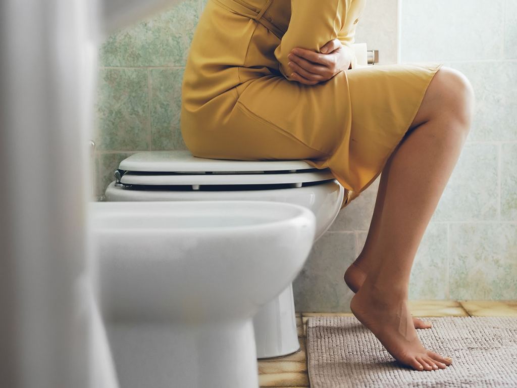 a woman in a yellow dress experiencing urinary discomfort while sitting on a toilet