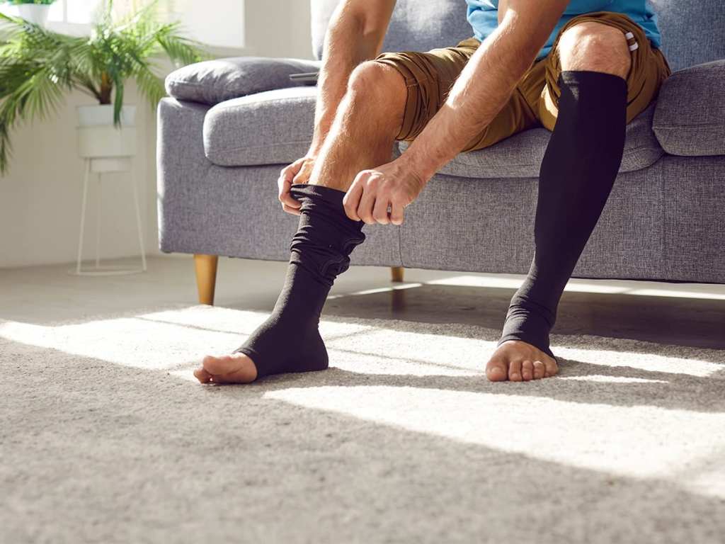 a man sitting on a couch, putting on compression stockings