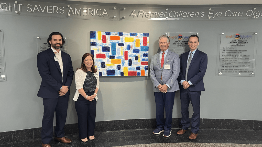 Logan Balandrin, Dianne Scalici, Michael Callahan, and Brian Samuels stand next to the 2026 Hall W. Thompson Hero for Sight tribute wall .
