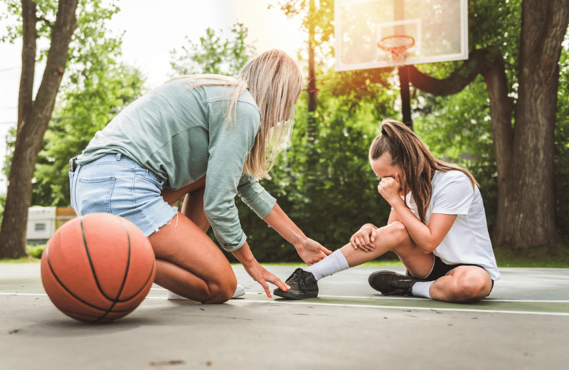 Mother and little daughter play basketball outside crying because of high ankle injury